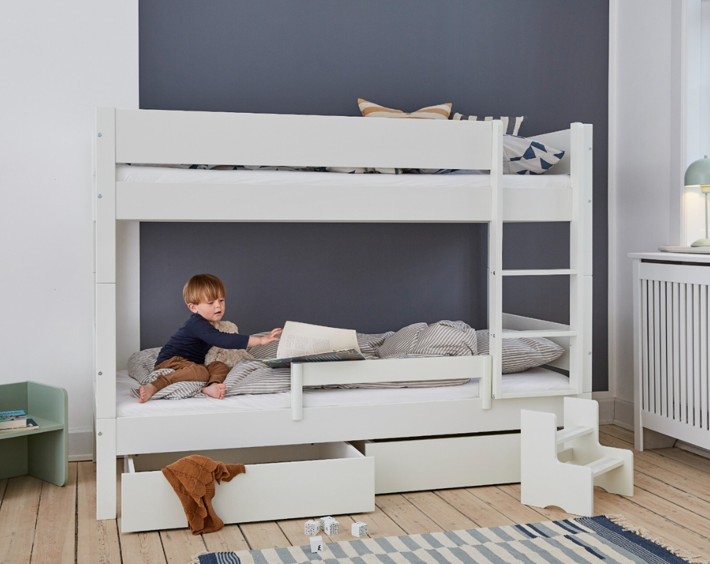 Hvid køjeseng med et barn der læser i den nederste køje, med sengehest og skuffer